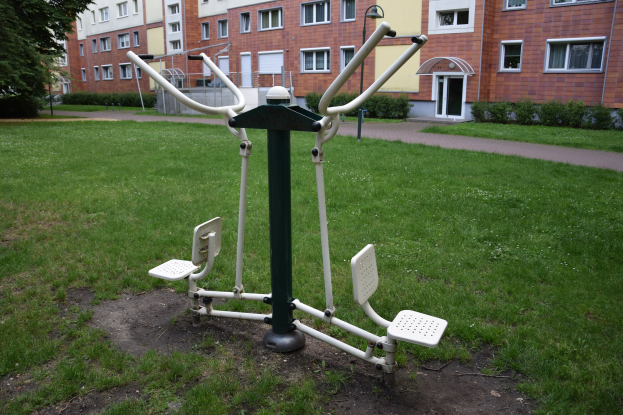 Outdoor-Gym-Ausrüstung in einer grünen Fläche mit Bäumen und Gebäuden im Hintergrund.