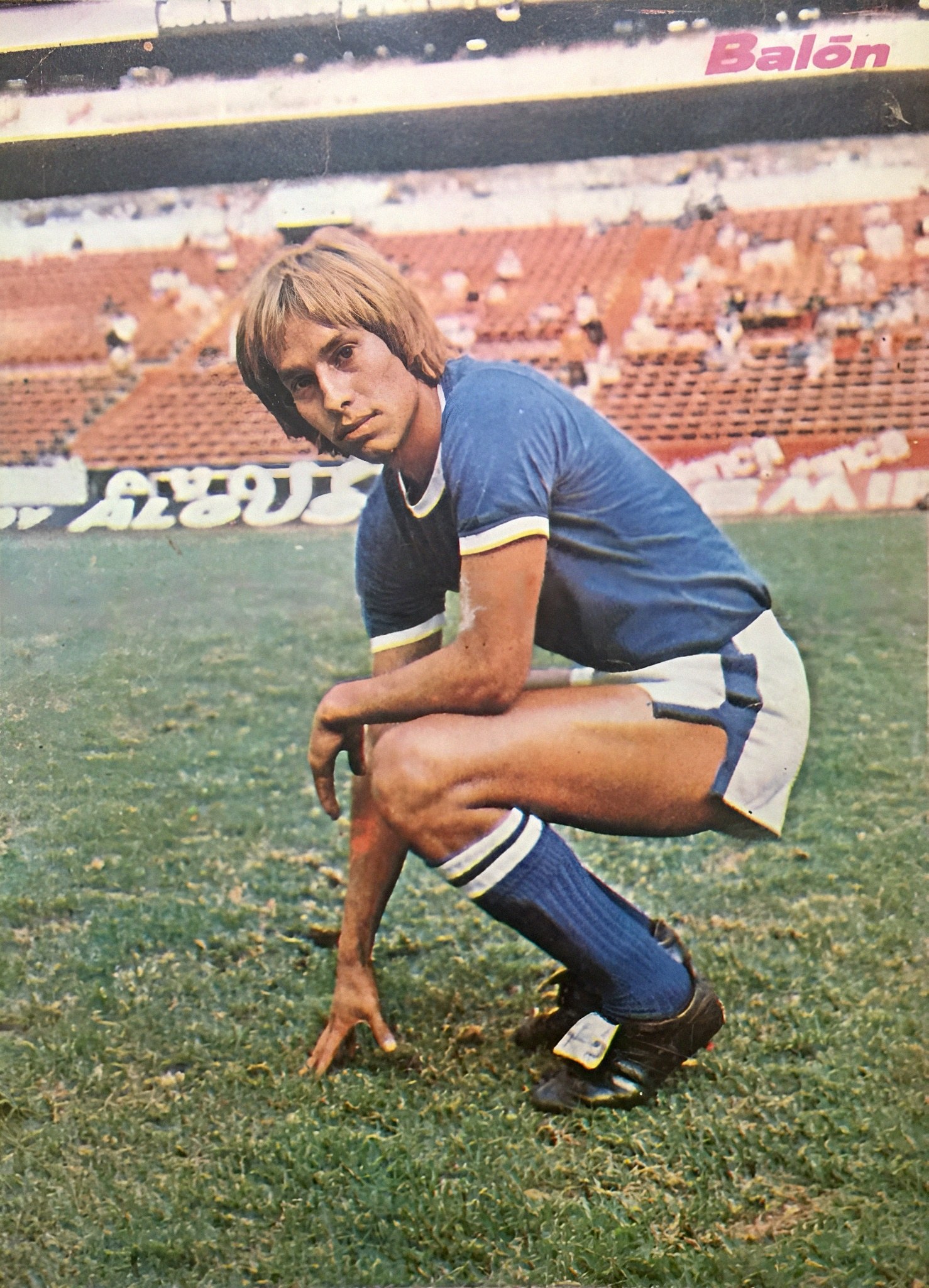 Ein Mann kniet auf einem Fußballfeld umgeben von sitzenden Personen mit Schildern, die Schuhe tragen.