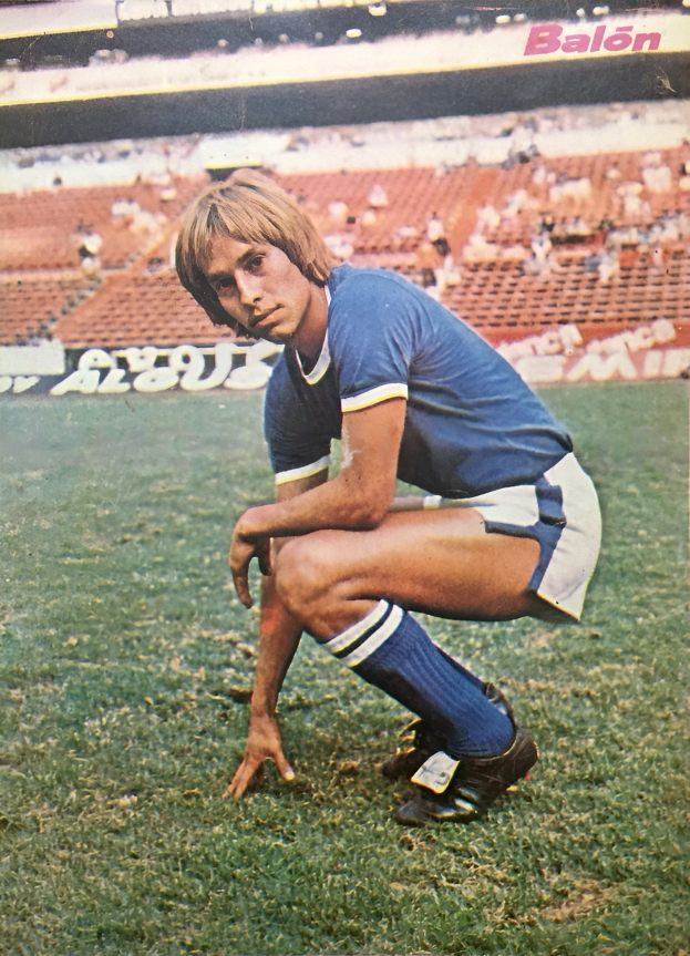 Ein Mann kniet auf einem Fußballfeld umgeben von sitzenden Personen mit Schildern, die Schuhe tragen.