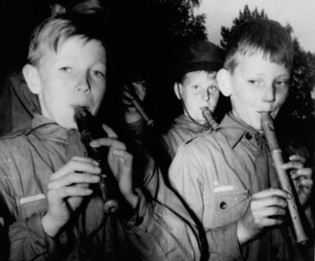 Gruppe junger Jungs, die Flöten im Freien spielen, Schwarz-Weiß-Bild mit Bäumen im Hintergrund.