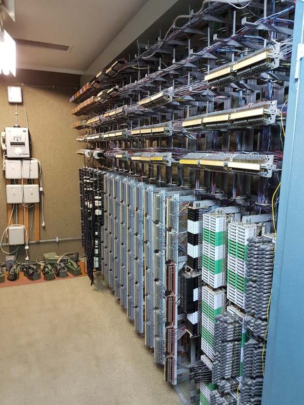 Großer Raum voller numerous wires, elektronische Geräte und Server auf dem Boden, mit einer Wand auf der linken Seite, was auf eine Rechenzentrumseinrichtung hinweist.