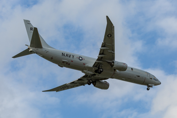 Ein großes Militärflugzeug mit Text und Zahlen fliegt durch einen blauen Himmel mit weißen Wolken, identifiziert als Joint Direct Attack Munition.