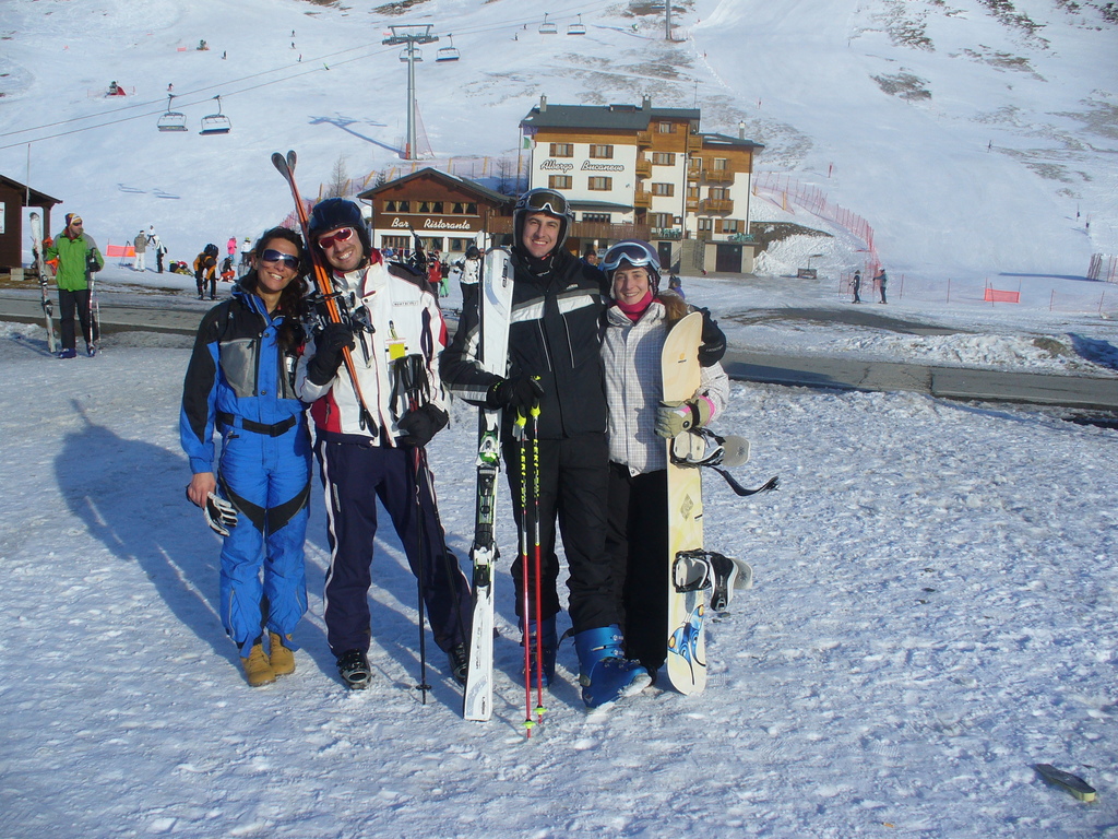Vier Personen posieren für ein Foto mit Skaterpads und Werkzeugen im Hintergrund vor einer schneebedeckten Berglandschaft.