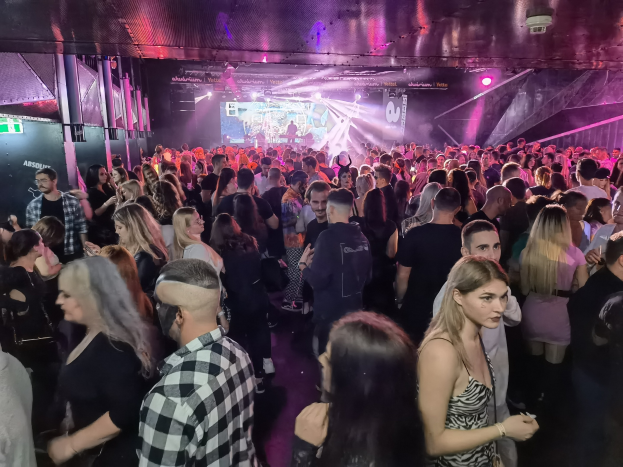Eine große Menschenmenge in einer Diskothek mit Deckenlichtern und Säulen, mit einem Bildschirm im Hintergrund, der als Absolut Nightlife-Event gekennzeichnet ist.