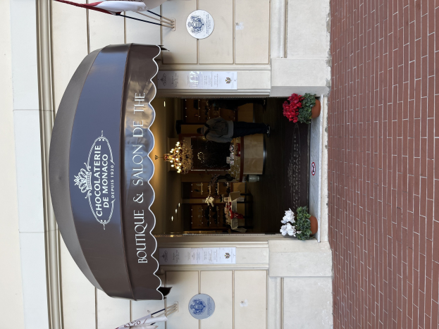 Ein Boutique- und Salon-Geschäft namens "Boutique & Salon de Monaco" mit Außenbereich, Topfpflanzen und einem durch Fenster sichtbaren beleuchteten Innenraum.