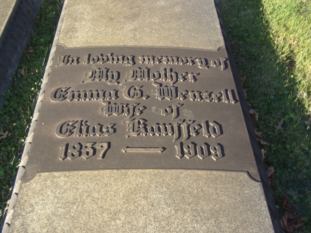 Grabstein auf einem Friedhof mit der Inschrift "In liebevoller Erinnerung meiner Mutter", umgeben von Gras und welken Blättern.