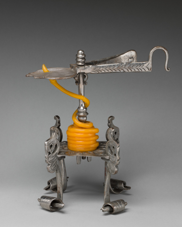 Ein metallener Korkenzieher mit einer hellgelben Feder an seiner Oberseite, der einen zylindrischen Körper, einen Griff auf einer Seite und einen Ausguss auf der anderen Seite aufweist.