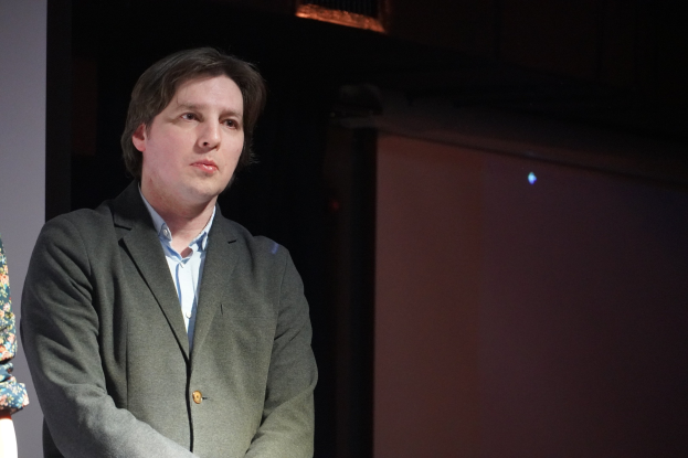 Ein Mann im Anzug und eine Frau stehen Seite an Seite auf einer Bühne, beide mit ernsten Gesichtern.