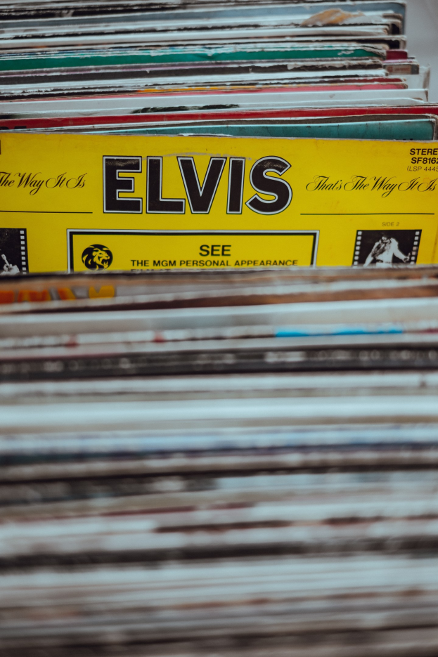 Ein ordentlicher Stapel Elvis-Presley-Platten auf einem Tisch, mit sichtbaren Titeln und einem unscharfen Hintergrund.