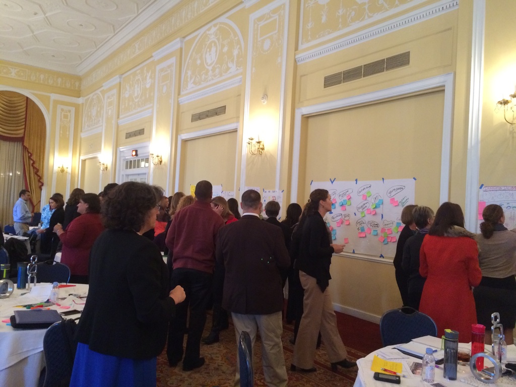 Eine Gruppe von Menschen betrachtet Plakate und Charts, die an einer Wand in einem Raum aufgehängt zu sein scheinen, der wie ein Kunstmuseum aussieht.