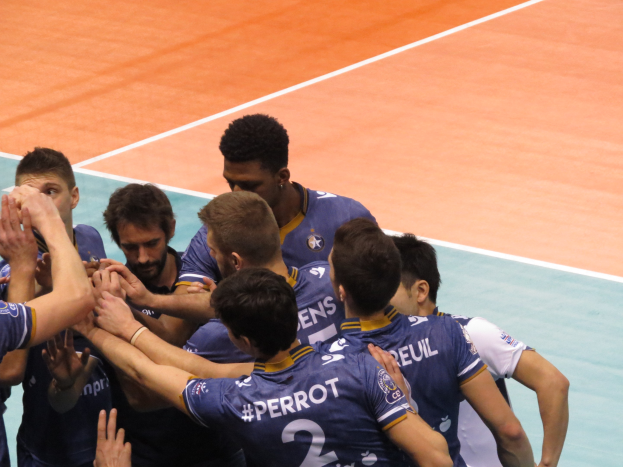 Gruppe von Männern in blauen "Ligue 1"-T-Shirts, die auf einem Volleyballfeld feiern, einige mit erhobenen Händen.