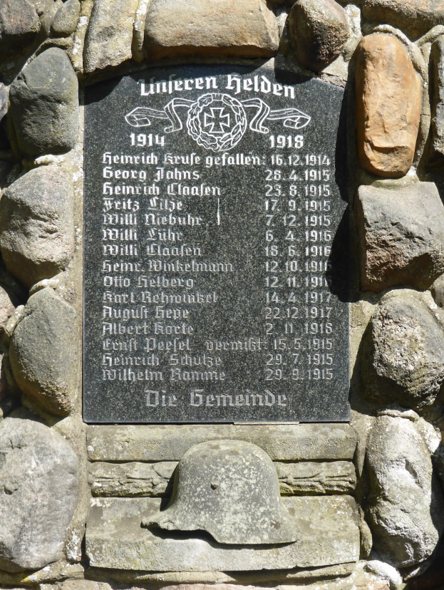 Steinwand mit Metalltafel mit eingravierter Schrift und einem Helm darauf, wahrscheinlich ein Weltkriegs-Denkmal der deutschen Wehrmacht.