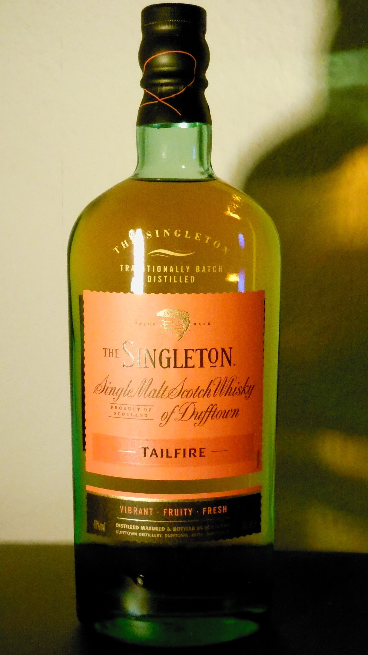 Eine tiefe bernsteinfarbene Flasche Singleton of Dufftown Tailfire Single Malt Scotch Whisky mit einem schwarzen Etikett, das eine schlagzeilenartige Schrift und ein Wappen mit einem Löwen und einer Burg zeigt.