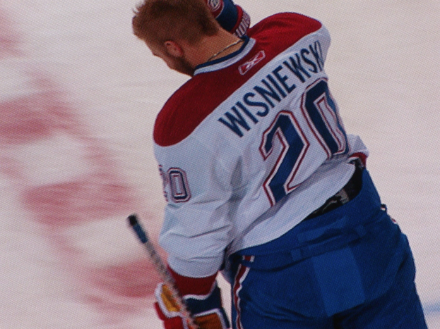 Professioneller Hockey-Spieler in einem "Wisniewski"-Trikot, der auf dem Eis steht und einen Hockey-Schläger hält, mit konzentrierter Miene.