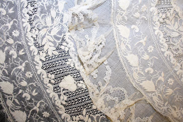 Nahaufnahme eines weißen Hochzeitskleids mit feiner Spitzenverzierung und zarten, variierenden Mustern auf einem leichten, luftigen Stoff.