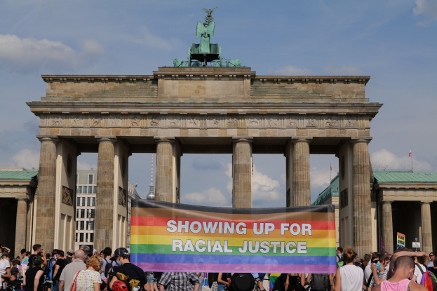 Eine Gruppe von Menschen steht vor dem Brandenburger Tor in Berlin, Deutschland, und hält ein Banner mit der Aufschrift "Racial Justice."