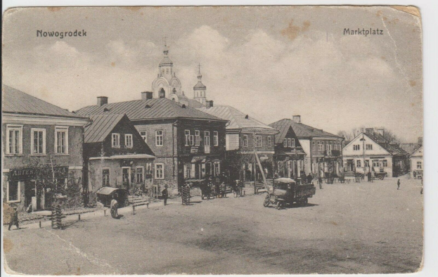 Schwarz-weiß-Foto einer Stadtstraße in Nowogrodziec, Deutschland, mit Gebäuden, Menschen, Karren, Pfählen, Bäumen und Himmel sowie dem Text "Marktplatz in Nowogrodeek, Deutschland" oben und unten.