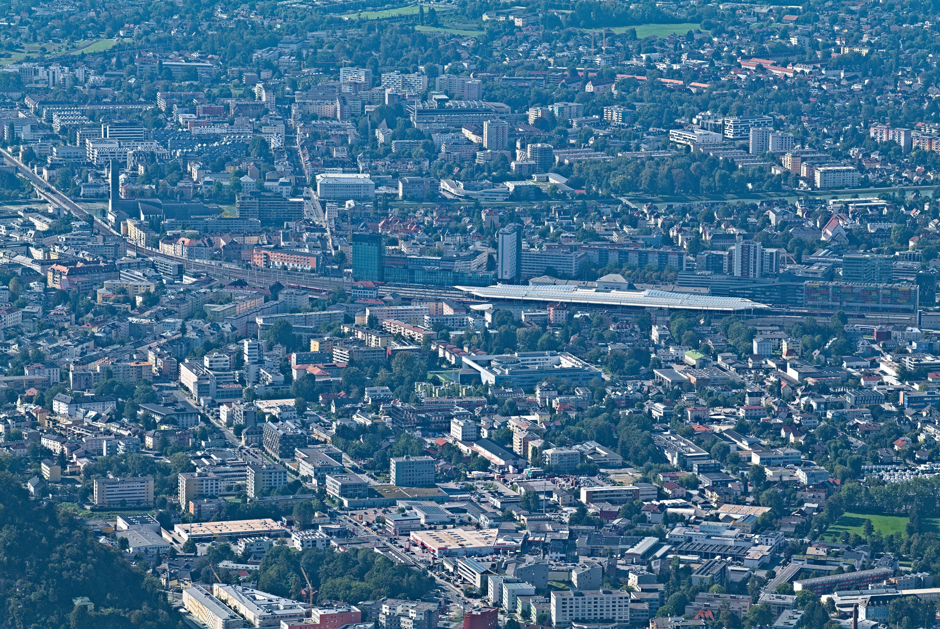 Eine Luftaufnahme einer belebten Stadt mit hohen, bunten Gebäuden, grünen Bäumen, gewundenen Straßen und saftig grünem Gras, mit Menschen, die spazieren gehen und Autos fahren.
