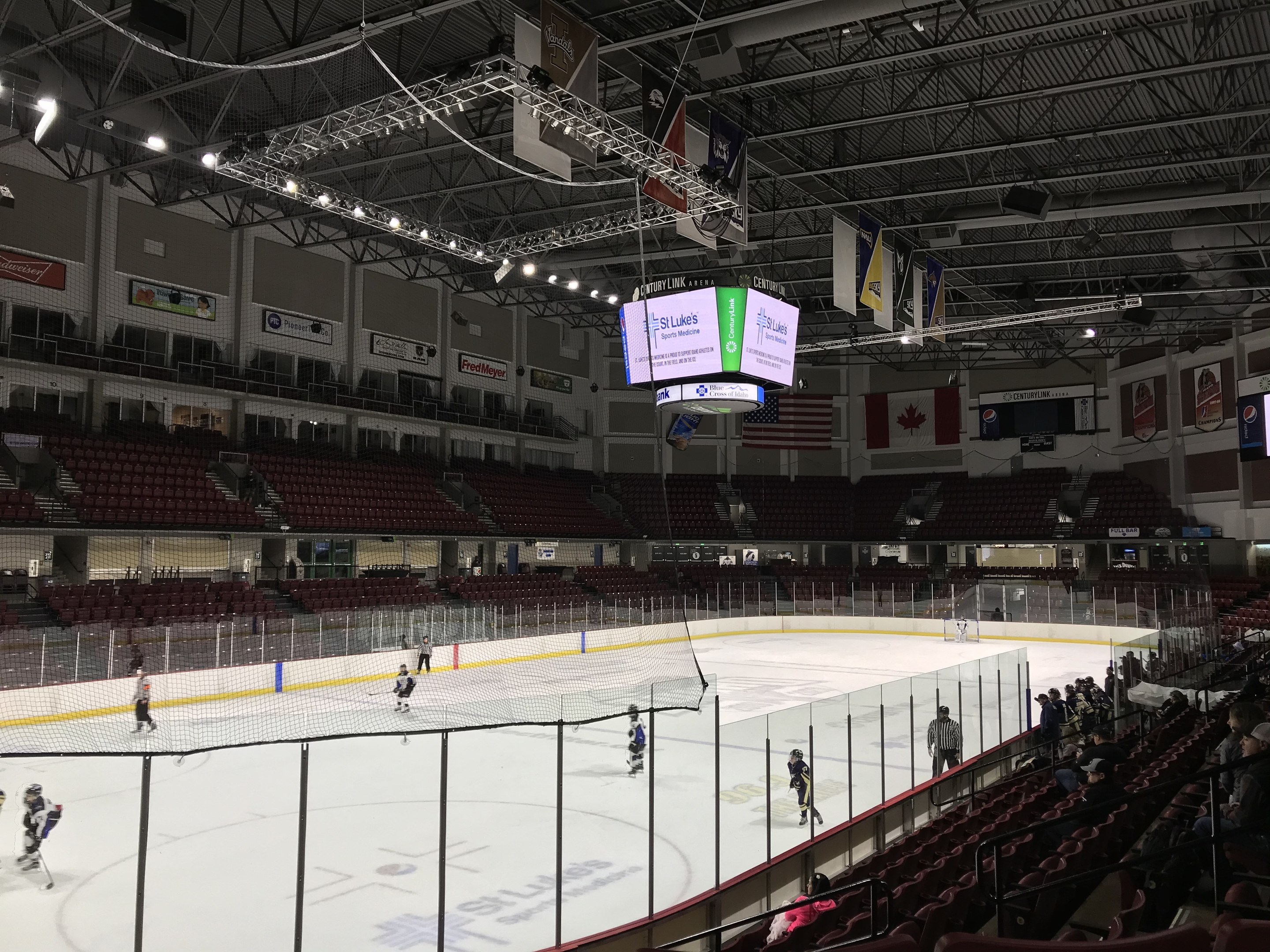 Hockeyspiel in einer großen Arena mit einem zentralen Netz, Zuschauern auf beiden Seiten, Deckenbeleuchtung und Trägern sowie Banner an den Wänden, die "St. Louis Blues Arena" beschriftet sind.