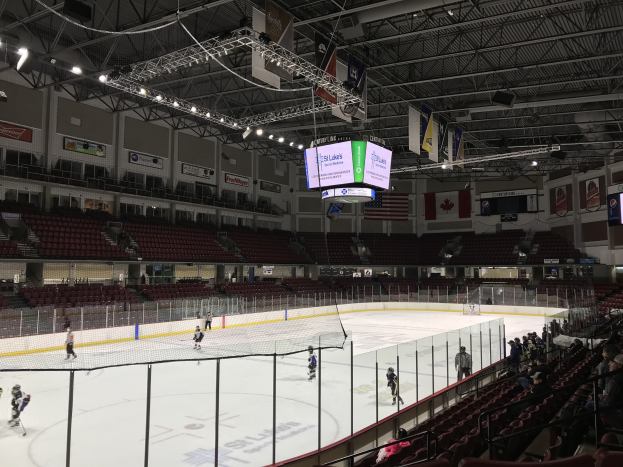 Hockeyspiel in einer großen Arena mit einem zentralen Netz, Zuschauern auf beiden Seiten, Deckenbeleuchtung und Trägern sowie Banner an den Wänden, die "St. Louis Blues Arena" beschriftet sind.
