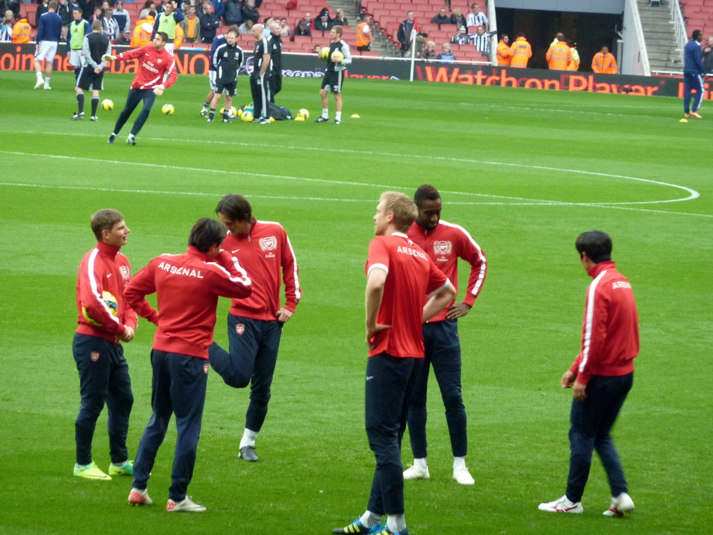 Eine Gruppe von Spielern, die auf einem grünen Feld mit Fußballschuhen stehen und ein Publikum im Hintergrund auf Stühlen sitzt.