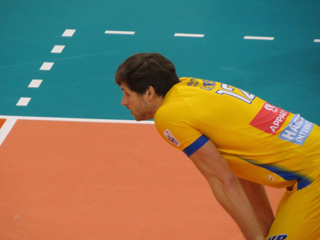 Eine professionelle Volleyballspielerin in einem gelben "Volleyball"-T-Shirt steht selbstbewusst auf einem Court und ist bereit zum Aufschlag.