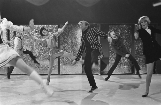 Eine Gruppe von Menschen, die auf einer Bühne tanzen, mit Schuhen bekleidet und mit einer Wand im Hintergrund, dargestellt in Schwarz-Weiß.