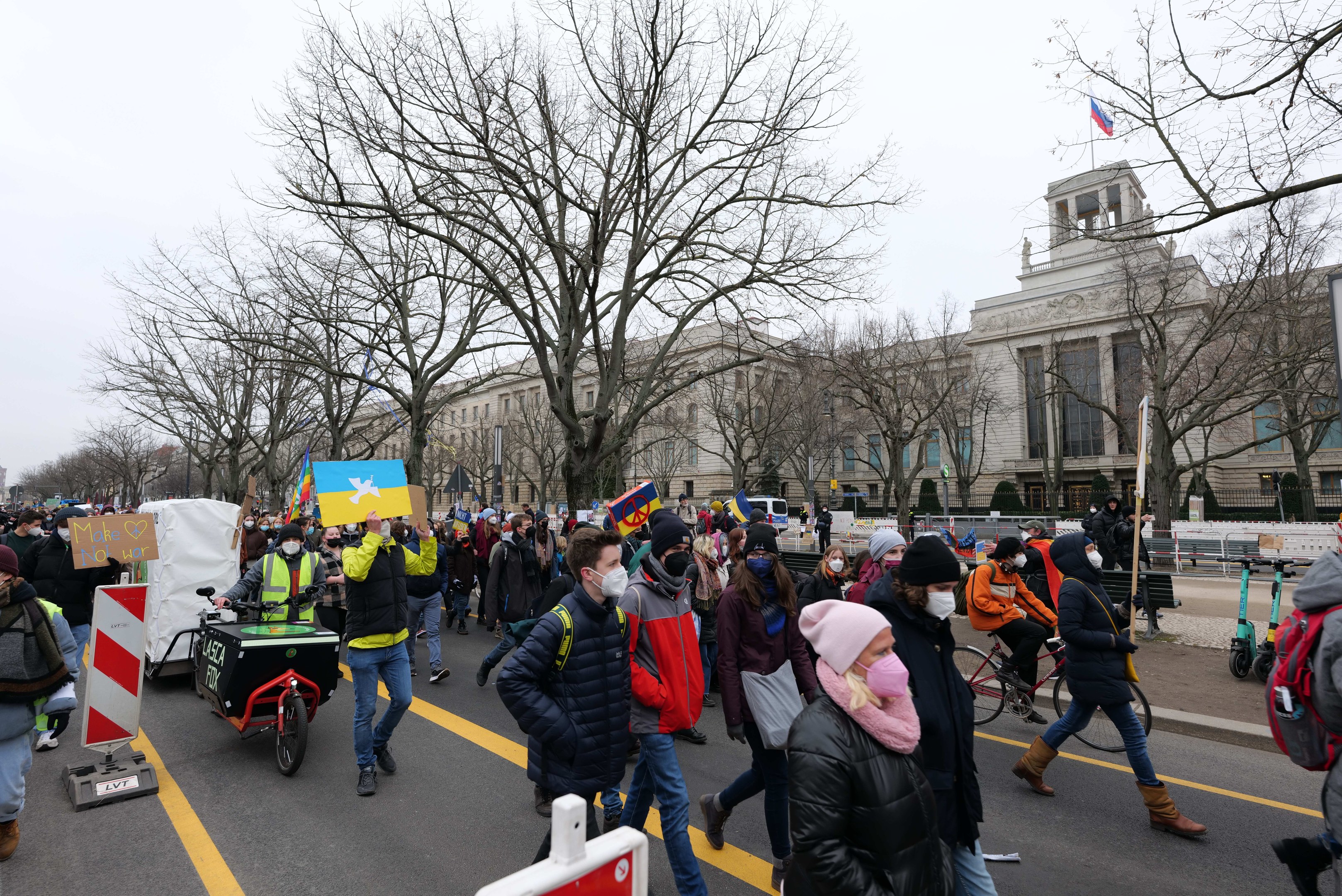 Eine große Gruppe von Menschen marschiert auf einer Demonstration in Washington, D.C., mit Schildern und Fahrrädern, mit Bäumen und einem klaren blauen Himmel im Hintergrund.