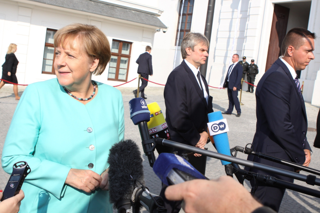 Bundeskanzlerin Angela Merkel spricht vor der Kanzleramt in Berlin mit Reportern, umgeben von Menschen mit Mikrofonen und Gebäuden im Hintergrund.