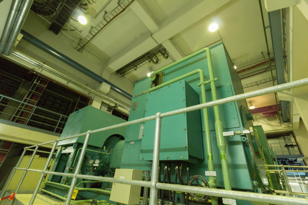 Großer industrieller Wärmetauscher in einem Gebäude umgeben von Geländern, Rohren, Ventilen und Beleuchtungsausrüstung.