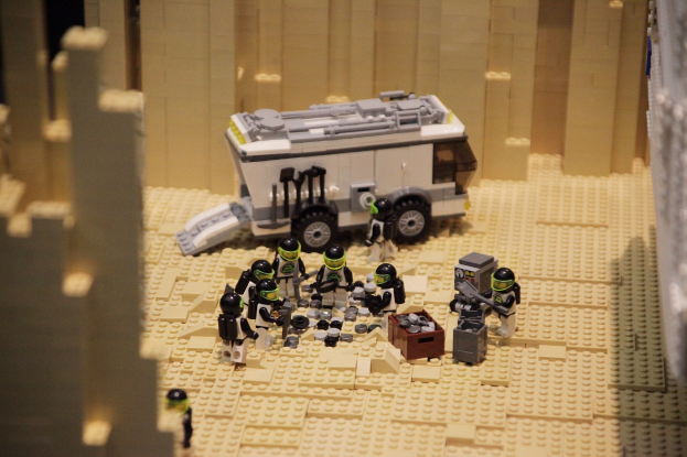 Lego-Modell einer Star Wars-Szene mit einem Landfahrzeug im Vordergrund und verstreuten Spielzeugen sowie einer Wand im Hintergrund.