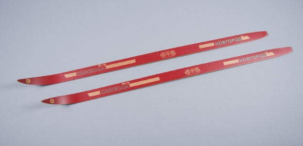 Zwei rote Ski übereinandergestapelt auf einer weißen Oberfläche mit Text, der die Marke oder das Modell angibt.