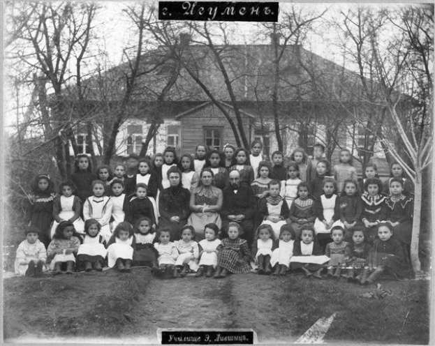 Schwarzes und weißes Foto einer Gruppe von Kindern, die vor einem Fensterbau mit Fenstern posieren, umgeben von Bäumen und einem klaren Himmel, mit Text unten, der 'Jugoslawien, die erste Schule der Welt' liest.