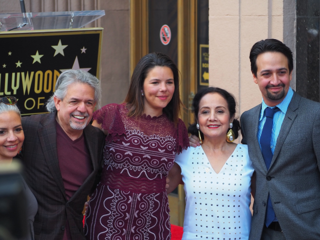 Gruppe von Menschen, die auf dem roten Teppich bei der Zeremonie des Hollywood Walk of Fame posen, mit einer Tafel, einer Glasvitrine und einer Wand im Hintergrund.
