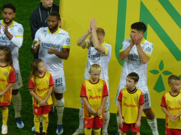 Eine Gruppe von Fußballspielern in Uniform klatscht auf einem Ligue 1-Feld in celebration, mit einem "Ligue 1" -Schild im Hintergrund.