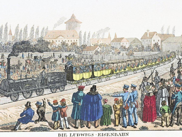 Eine Gruppe von Menschen steht um einen Zug auf einem Gleis herum, einige sitzen im Zug, andere stehen daneben, in der Nähe von Gebäuden und Bäumen, mit dem Text "Ludwigs-Eisenbahn, der erste Bahnhof in Deutschland" unten.