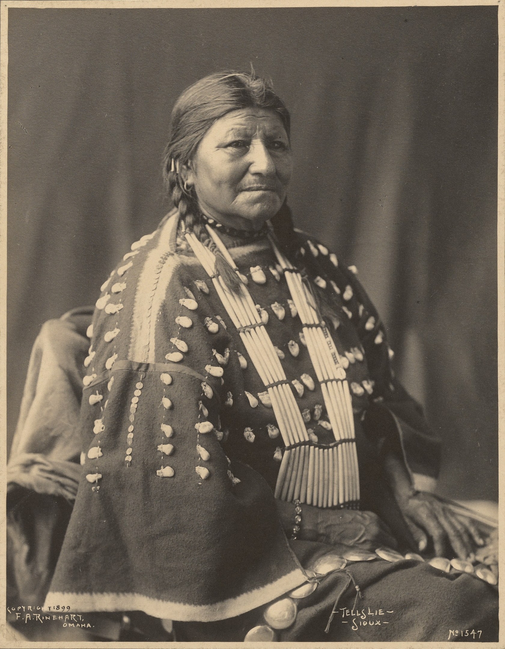 Ein Schwarz-Weiß-Foto einer indischen Frau in traditioneller Kleidung mit ernstem Gesichtsausdruck, gefalteten Händen, zurückgebundenem Haar und einer Federhaube.