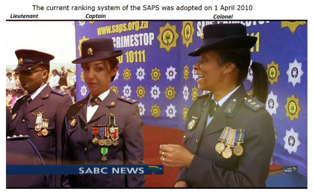 Eine Gruppe von Menschen in Uniformen und Hüten steht mit einem Banner im Hintergrund, mit Text oben und unten, der lautet "Das aktuelle Ranglistensystem der SAP wurde am 1. April 2010 eingeführt."