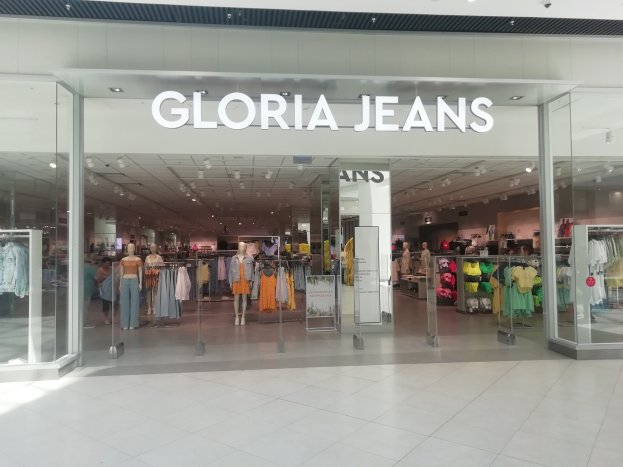 Innenansicht eines Gloria Jeans Stores in einem Einkaufszentrum, mit Schaufensterpuppen in moderner Kleidung, aufgehängten Kleidungsstücken und Deckenbeleuchtung, sowie sichtbarem Ladengeschoss.