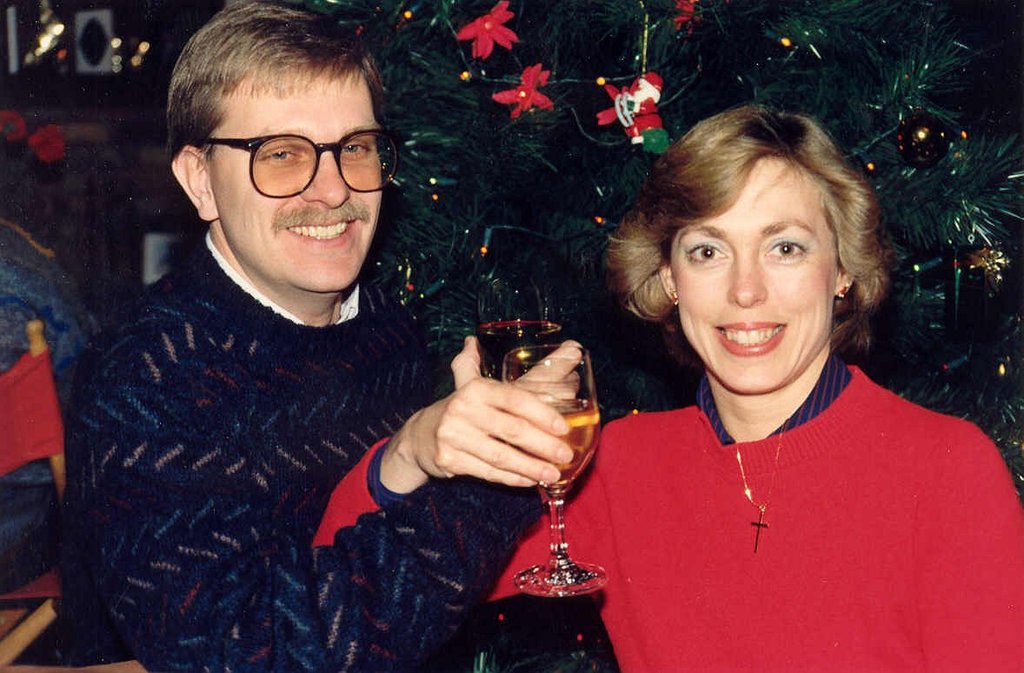 Ein Paar lächelt, waßrend es Gläser Wein hält, mit einem Weihnachtsbaum im Hintergrund.