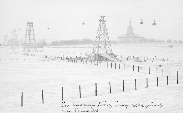 Schwarze-Weiß-Foto eines Skilifts in einem verschneiten Feld mit Stützpfählen, Überseilbahn, Bäumen und einem Gebäude im Hintergrund, mit Text unten.