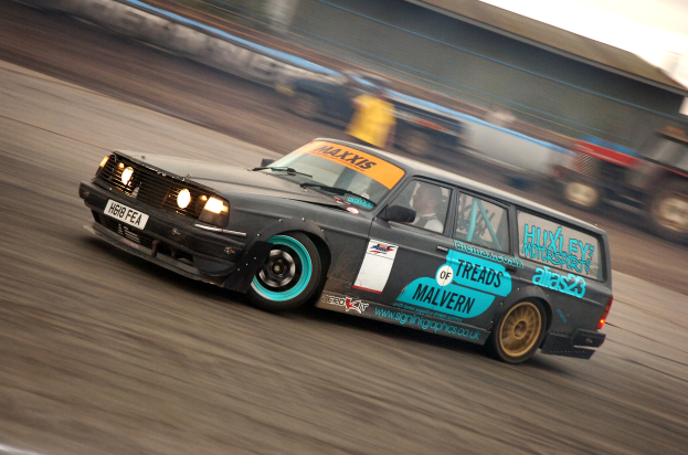Ein Auto rast auf einer Rennstrecke mit einem Fahrer darin, umgeben von anderen Fahrzeugen, mit einem unscharfen Hintergrund, der hohe Geschwindigkeit andeutet.