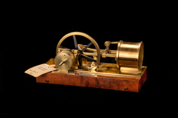 Altmodische Uhr mit einem Holzunterbau, Metallrad und einem Papier-Zeitschalter, vor einem schwarzen Hintergrund.