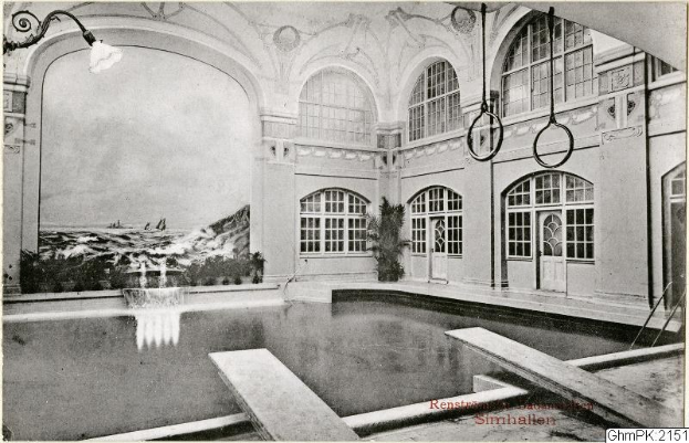 Altes Schwarz-Weiß-Foto eines großen Hallenbads in Rensburg, Deutschland, mit Glasfenstern, Pflanzen und einer Hängelampe.