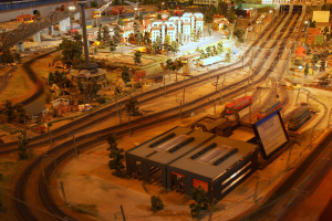 Eine Modellbahnanlage in einem Museum mit Gebäuden, Bäumen, Eisenbahnschienen, Fahrzeugen, Pfählen, Lichtern, Platten und anderen Gegenständen, die eine lebhafte Stadtkulisse schaffen.