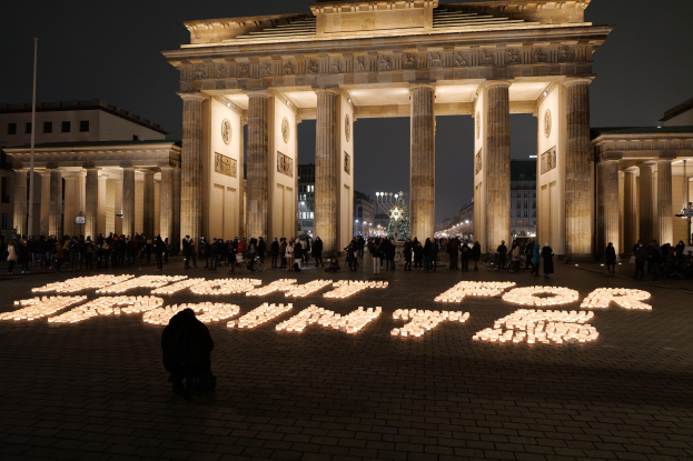 Eine Gruppe von Menschen steht vor dem beleuchteten Reichstagsgebäude in Berlin, Deutschland, umgeben von Gebäuden, Pfählen und Lichtern, und die Wörter 'Kampf für die Freiheit' sind auf dem Boden zu sehen.