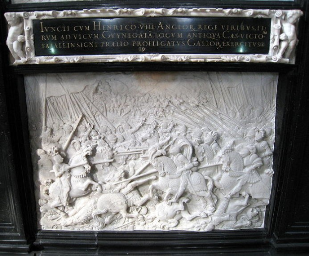 Weißer Marmorstein mit schwarzem Rahmen an einem Gebäude, der eine Schlachtenszene mit Schwert- und Schildhaltenden Figuren zeigt, umgeben von Zuschauern.