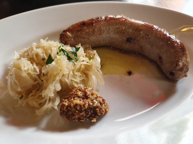 Ein weißer Teller, der mit Sauerkraut, deutscher Wurst und anderen Speisen garniert ist, in einer Nahaufnahme auf einem Tisch gezeigt.