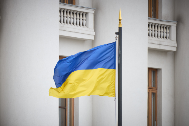 Die ukrainische Flagge weht an einem Mast vor einem mehrstöckigen Gebäude mit Fenstern und Geländern.