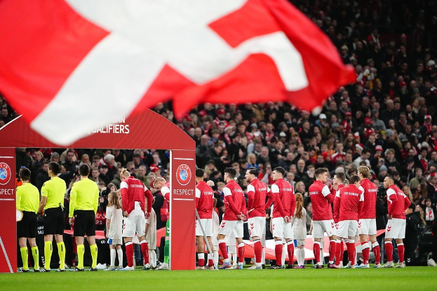 Gruppe von Menschen auf einem Fußballfeld mit einer roten und weißen Flagge im Vordergrund, einem Bogen mit der Aufschrift "Bayern Munich vs. Bayern Munich Wett-Tipps & Vorschau" im Hintergrund und einer großen Menschenmenge im Stadion.